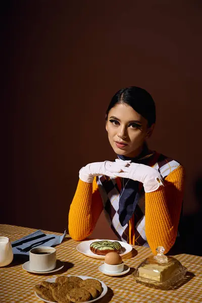 Una joven vestida con un atuendo retro se sienta en una mesa con un plato de galletas, un huevo y un donut glaseado.. — Stock Photo