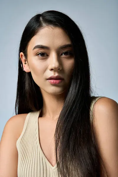 A young woman with long, dark hair poses confidently in a cream-colored, ribbed tank top. — Stock Photo