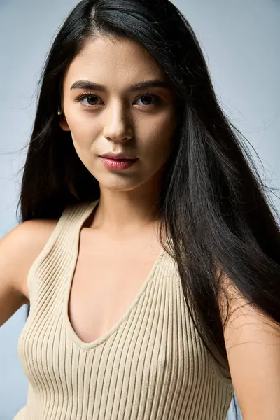 A young woman with long black hair poses in a light beige ribbed tank top. — Stock Photo