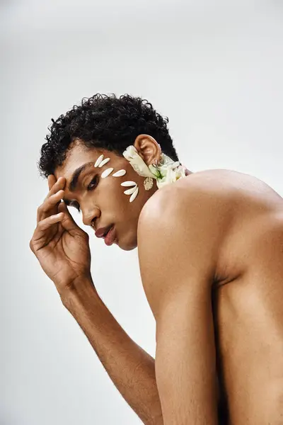 A young, muscular African American man poses with flowers on his face and body against a gray background. — Stock Photo