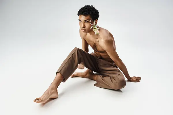A young African American man adorned with flowers poses confidently on a grey background. — Stock Photo