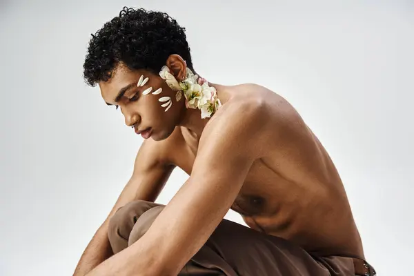 African American man sits adorned with white flowers on a grey backdrop, showcasing beauty and diversity. — Stock Photo