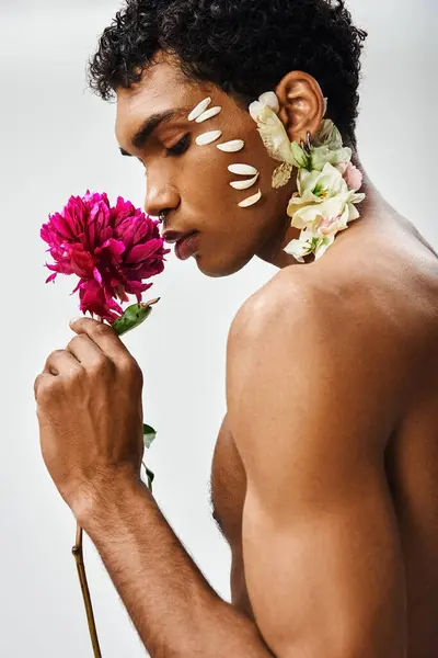 A young, muscular African-American man, adorned with flowers, poses against a gray background, showcasing beauty and diversity. — Stock Photo