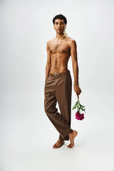 A young, muscular African American man poses with flowers on his body and face against a grey background. — Stock Photo