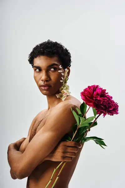 A young, muscular African American man stands with flowers adorning his body and face, against a neutral gray background. — Stock Photo