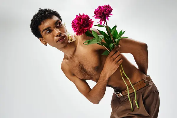 Ein junger, muskulöser afroamerikanischer Mann posiert mit Blumen auf Körper und Gesicht vor grauem Hintergrund. — Stockfoto