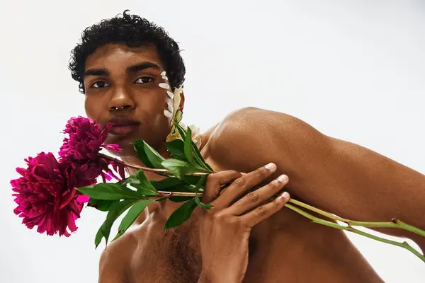 Um jovem afro-americano com flores adornando seu corpo e rosto, posando contra um fundo cinza. — Stock Photo