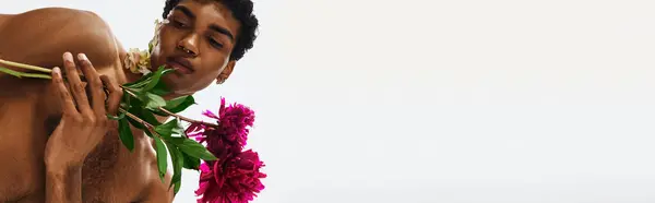 A young African American man with a muscular physique poses against a grey backdrop, adorned with flowers on his body and face. — Stock Photo