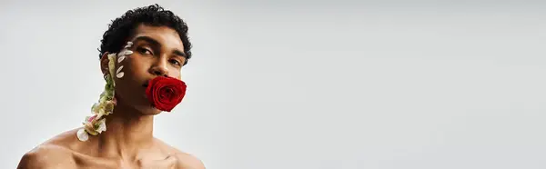 A young, muscular African American man poses against a gray background, adorned with delicate flowers. — Stock Photo