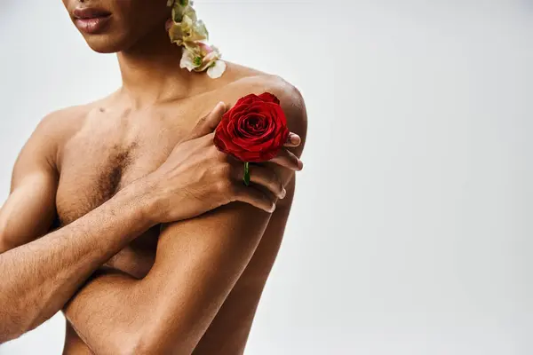 A confident African American man stands against a grey backdrop adorned with flowers, showcasing beauty and diversity. — Stock Photo