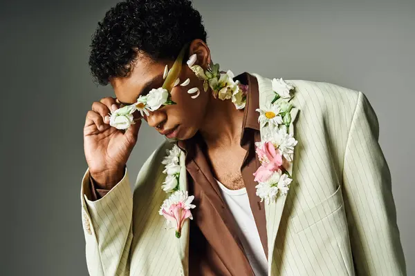 Un joven afroamericano con una elegante chaqueta adornada con flores posa sobre un fondo gris. — Stock Photo