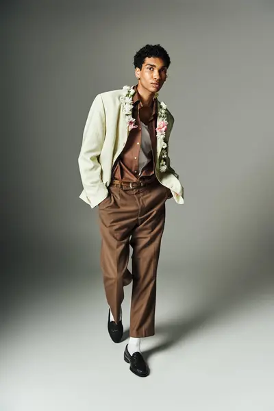 Um jovem afro-americano em um blazer elegante adornado com flores posa contra um fundo cinza. — Fotografia de Stock