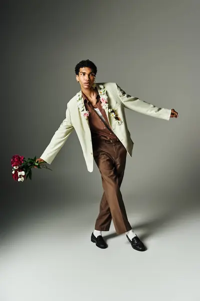 Un giovane uomo afroamericano in un blazer elegante decorato con fiori posa su uno sfondo grigio, incarnando bellezza e diversità. — Foto stock