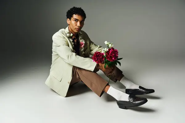 A young African American man in a stylish blazer sits with a bouquet of flowers. — Stock Photo