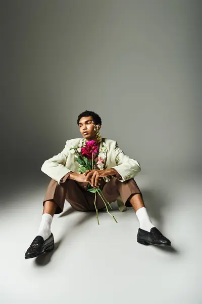 A young African American man in a stylish blazer poses with flowers around his neck showcasing beauty and diversity in fashion. — Stock Photo