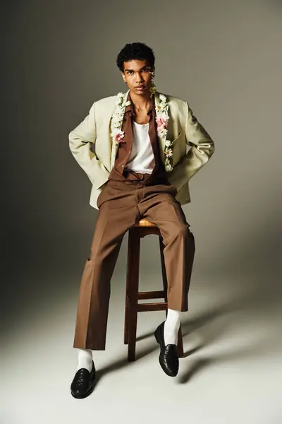 A young African American man poses stylishly in a blazer, adorned with flowers, on a grey background. — Stock Photo