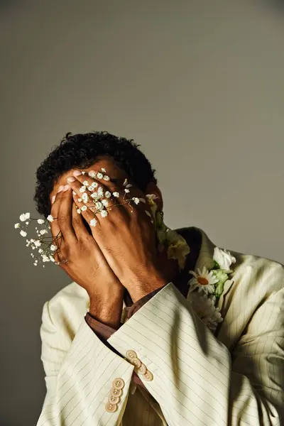 A young African American man poses in a stylish blazer, adorned with flowers, against a grey background. — Stock Photo