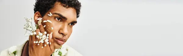 A young African American man poses against a grey backdrop, his face and neck adorned with white flowers, showcasing beauty and diversity. — Stock Photo