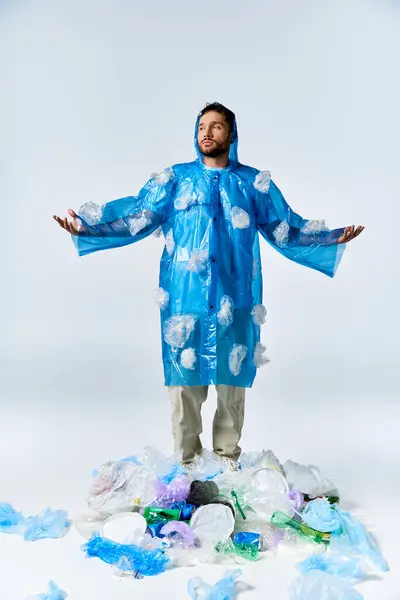 Homem de capa de chuva azul fica na pilha de plástico, braços estendidos. — Fotografia de Stock