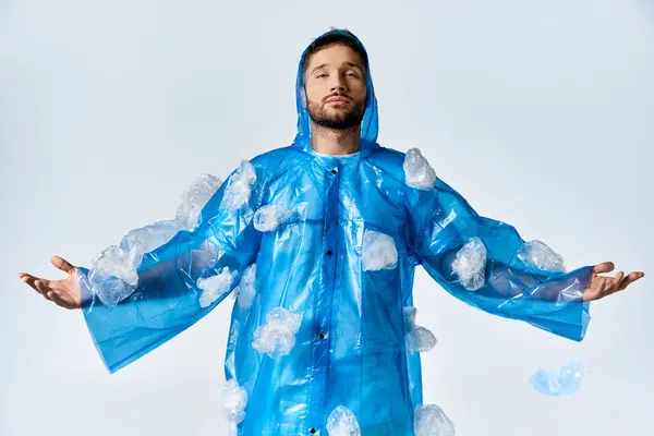 Man stands wearing blue plastic poncho and bags against plain background. — Stock Photo