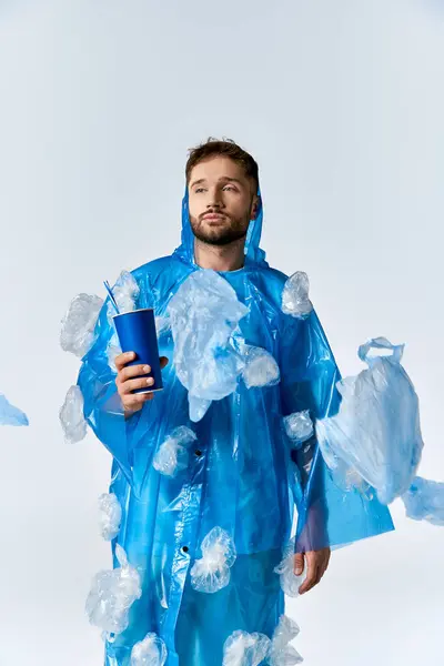 A man stands in a plastic raincoat with plastic bags attached to his clothing, holding a blue cup. — Stock Photo
