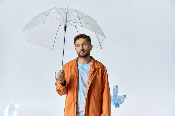 Um homem com uma jaqueta laranja está sob um guarda-chuva claro, com objetos de plástico ao seu redor. — Fotografia de Stock