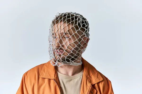 A man in an orange jacket stares into the distance, his face covered by a net. — Stock Photo