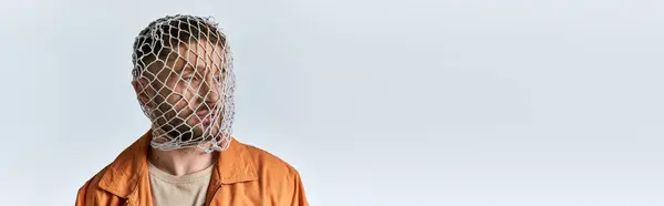 Um homem está contra um pano de fundo branco, sua cabeça coberta de uma rede de plástico, sua expressão sombria. — Fotografia de Stock