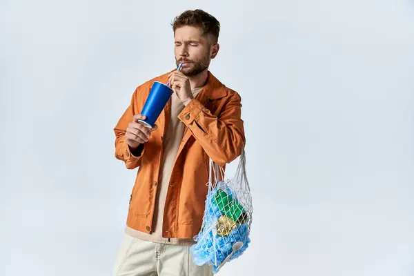 Um homem bebe de um copo de plástico, carregando um saco cheio de itens de plástico. — Fotografia de Stock