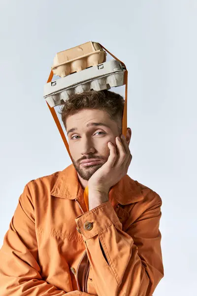 A man in an orange jacket wears an egg carton on his head. — Stock Photo