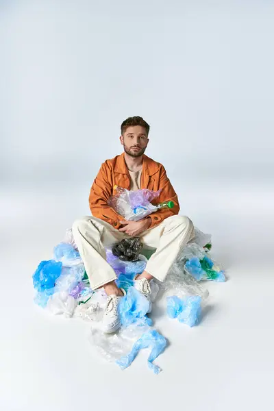 A man sits on a pile of plastic waste, surrounded by bags and bottles. — Stock Photo