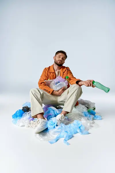 A man sits in a pile of plastic bags, holding a bottle and looking forlorn. — Stock Photo