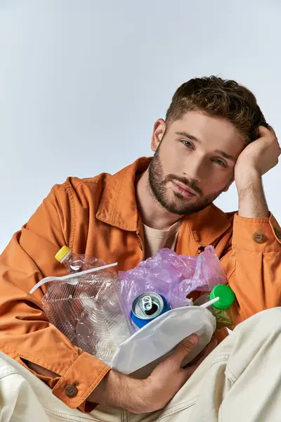 A man sits with his head in his hand, surrounded by plastic waste. — Stock Photo