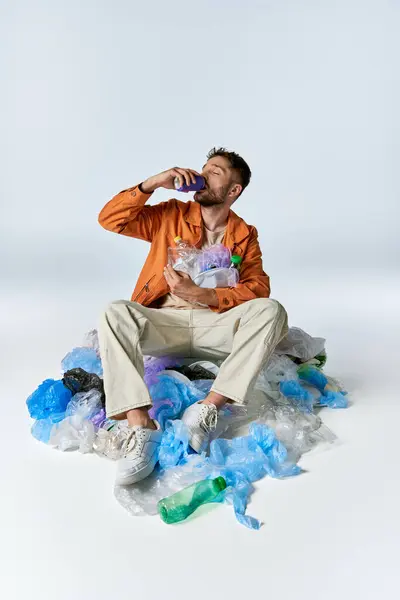 A man sits surrounded by a sea of plastic waste, drinking from a can. — Stock Photo