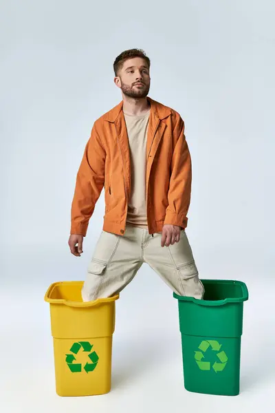 A man in an orange jacket is stuck with his legs in two recycling bins. — Stock Photo
