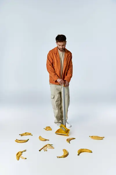 Um homem em uma roupa casual varre um círculo de cascas de banana com uma vassoura e pó. — Fotografia de Stock