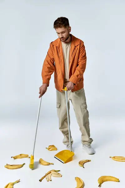 A man in an orange jacket cleans up banana peels on a white floor. — Stock Photo