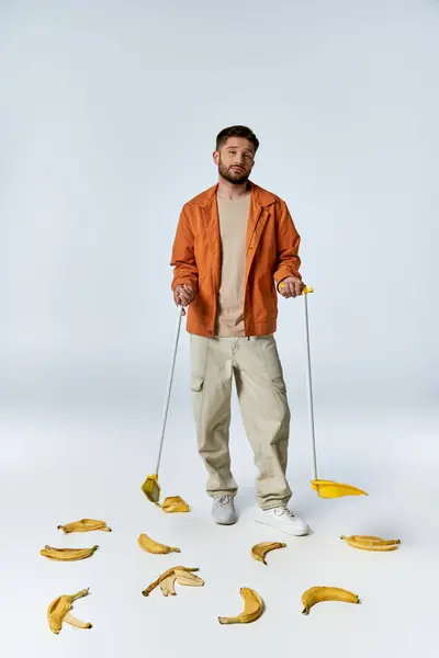 A man in an orange jacket stands on a white backdrop surrounded by banana peels. — Stock Photo
