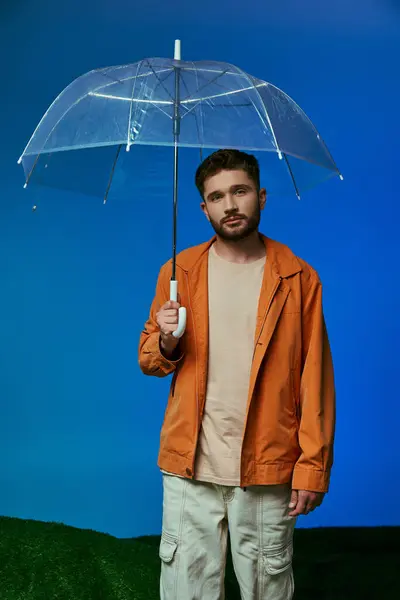 Un homme se tient dans un studio tenant un parapluie transparent, sur fond bleu. — Photo de stock