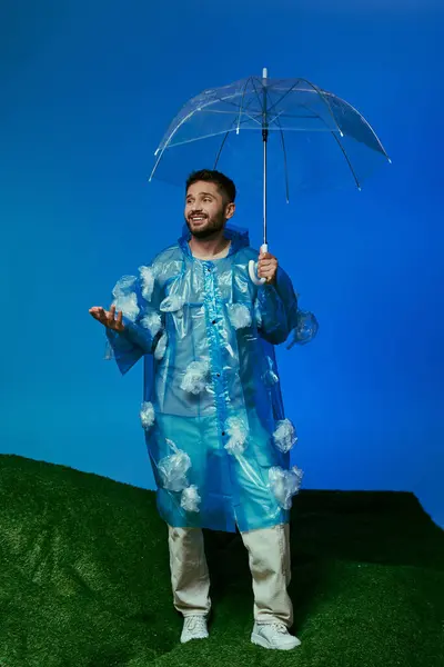 Un homme en imperméable en plastique tient un parapluie et pose sur une colline herbeuse. — Photo de stock