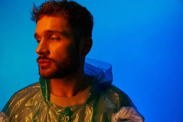 A handsome man poses against a blue background, wearing a plastic jacket. — Stock Photo