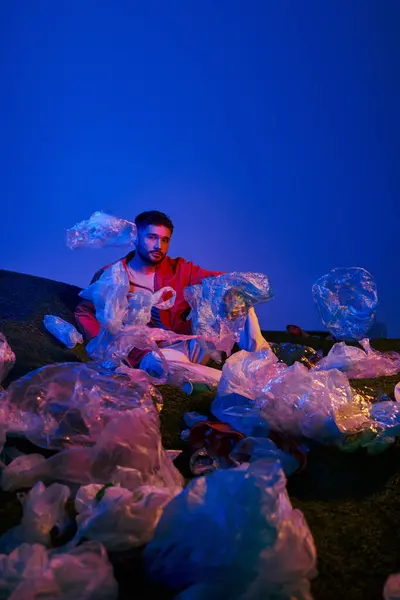 A man sits in a field of plastic bags, lit by a blue and red light. — Stock Photo