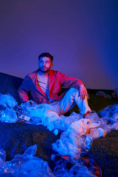 A man sits surrounded by plastic bags and bottles, illuminated by blue and purple lights. — Stock Photo