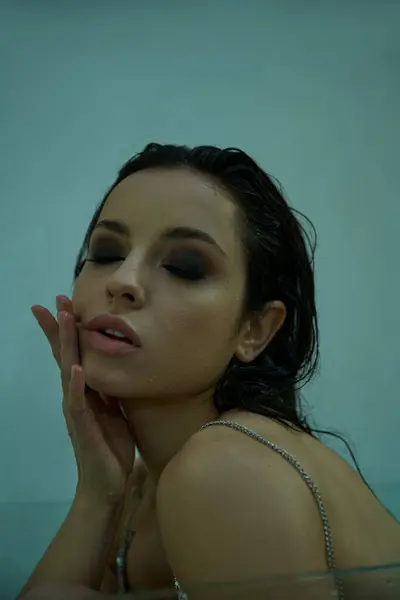 A young woman with wet hair emerges from the water in an underwater setting, her eyes closed and hands resting on her cheek. — Stock Photo