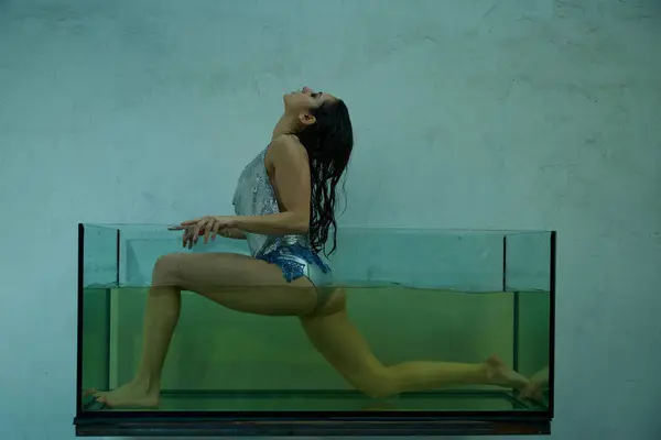 A young woman with wet hair stretches in a large glass tank, water level reaching her waist. — Stock Photo