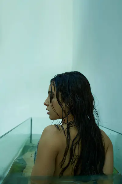 A beautiful young woman with wet, dark hair sits in an aquarium. — Stock Photo
