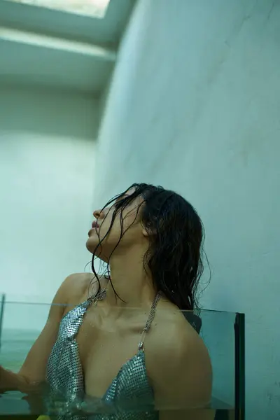 A young woman with wet brunette hair submerged in water, wearing a silver chainmail top, gazes upwards in an aquarium setting. — Stock Photo