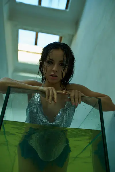 Uma jovem mulher com cabelo molhado e escuro posa em um top prateado cintilante, submersa em um aquário cheio de água. — Fotografia de Stock