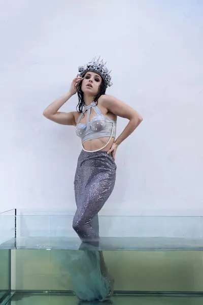 A young woman in a mermaid costume stands in a glass tank filled with water, her tail shimmering. — Stock Photo