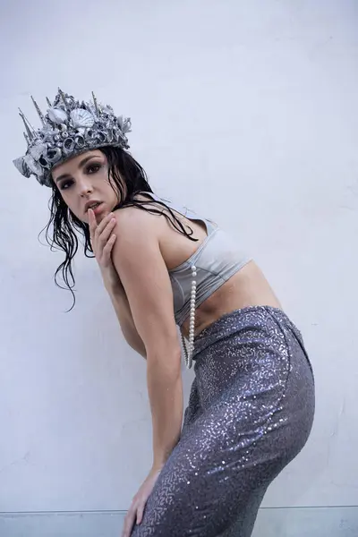 A young woman with long, wet hair wears a silver crown and a shimmering, sequined tail. — Stock Photo